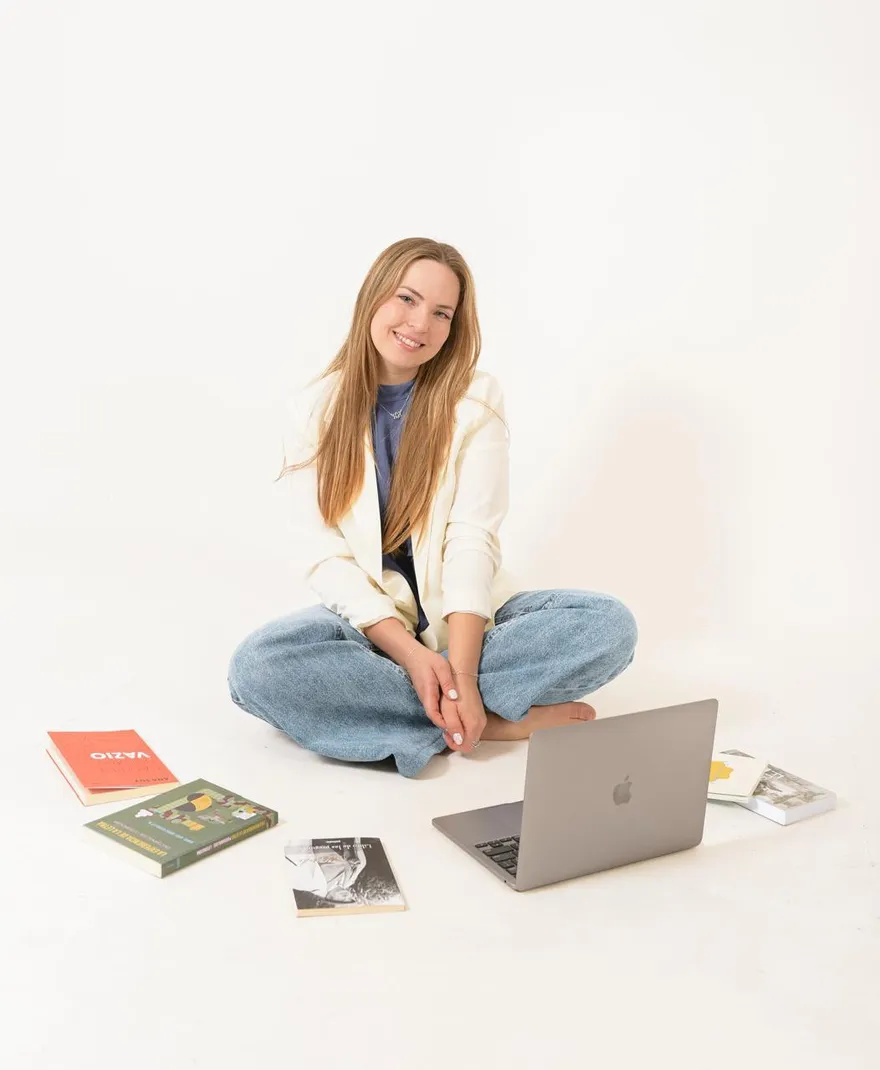 Mariana Marchetti sentada no chão, sorrindo, com livros e notebook ao redor